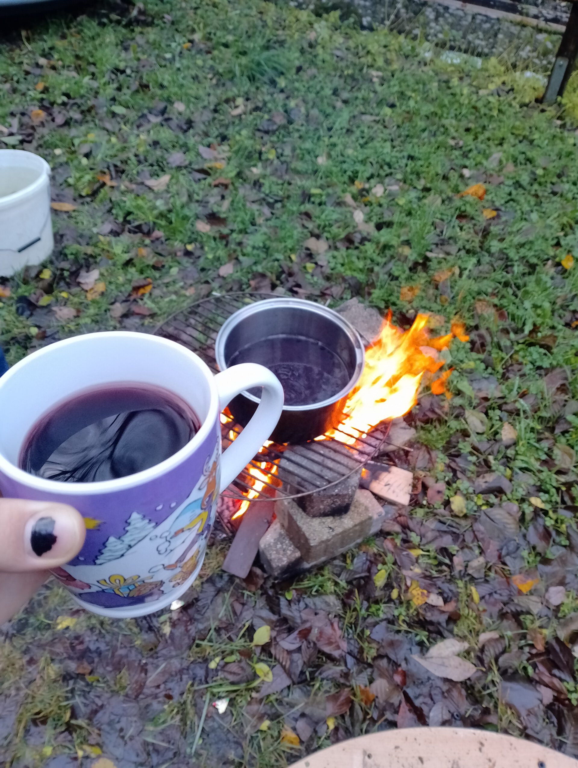 Eine Tasse und ein Topf mit Glühwein über dem Feuer