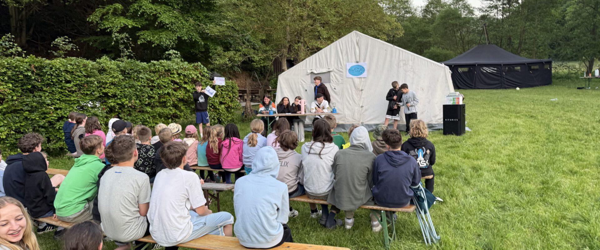 Pfingstlager 2026 5 Pfadfinder sitzen beim Bunten Abend draußen auf Bänken